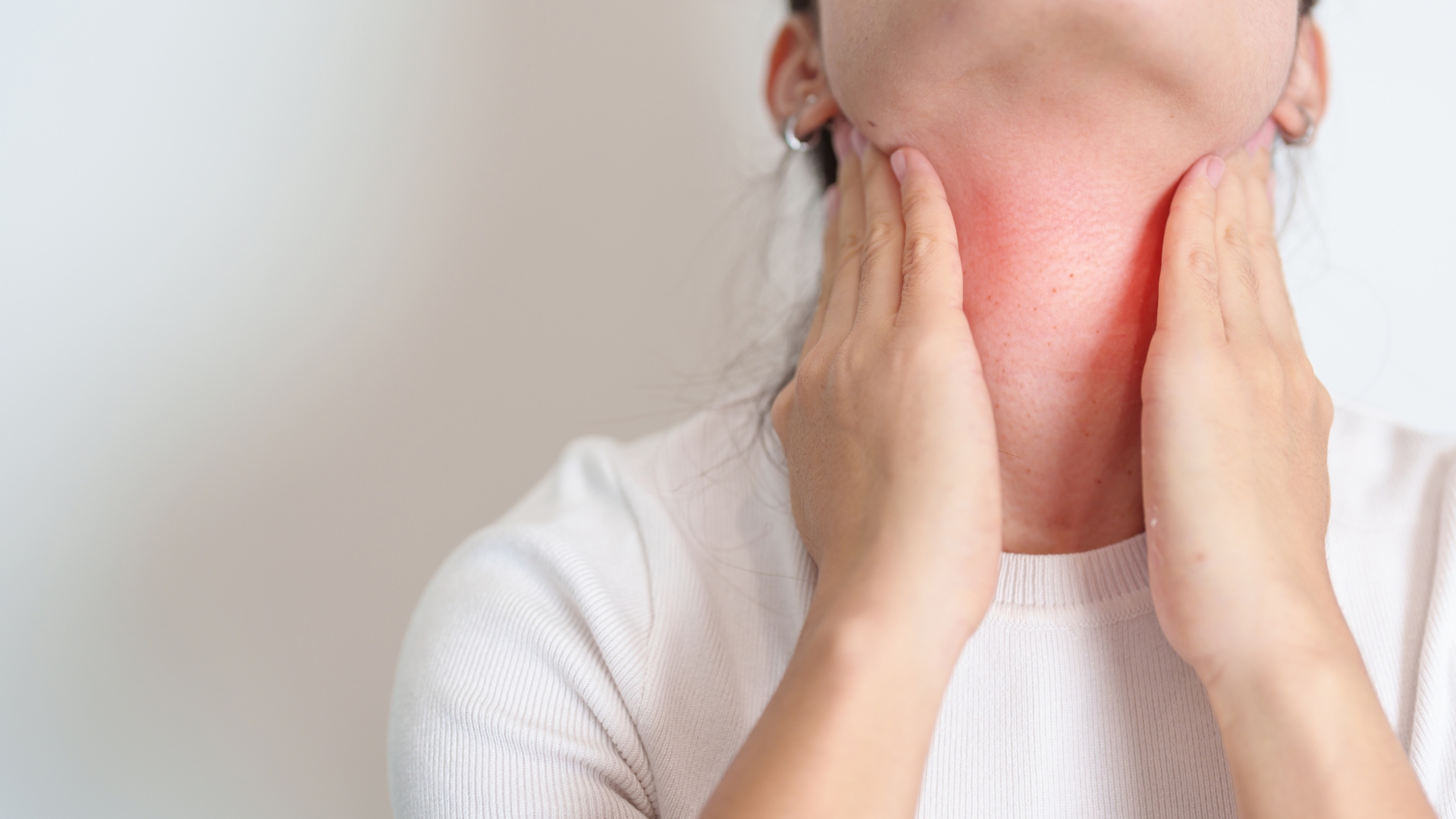 woman experiencing postpartum thyroiditis holding neck